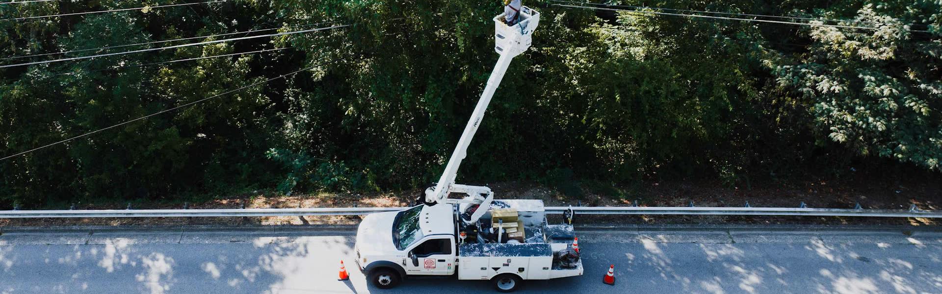Aerial view of a service crew bucket truck stopped on a tree-lined residential road.