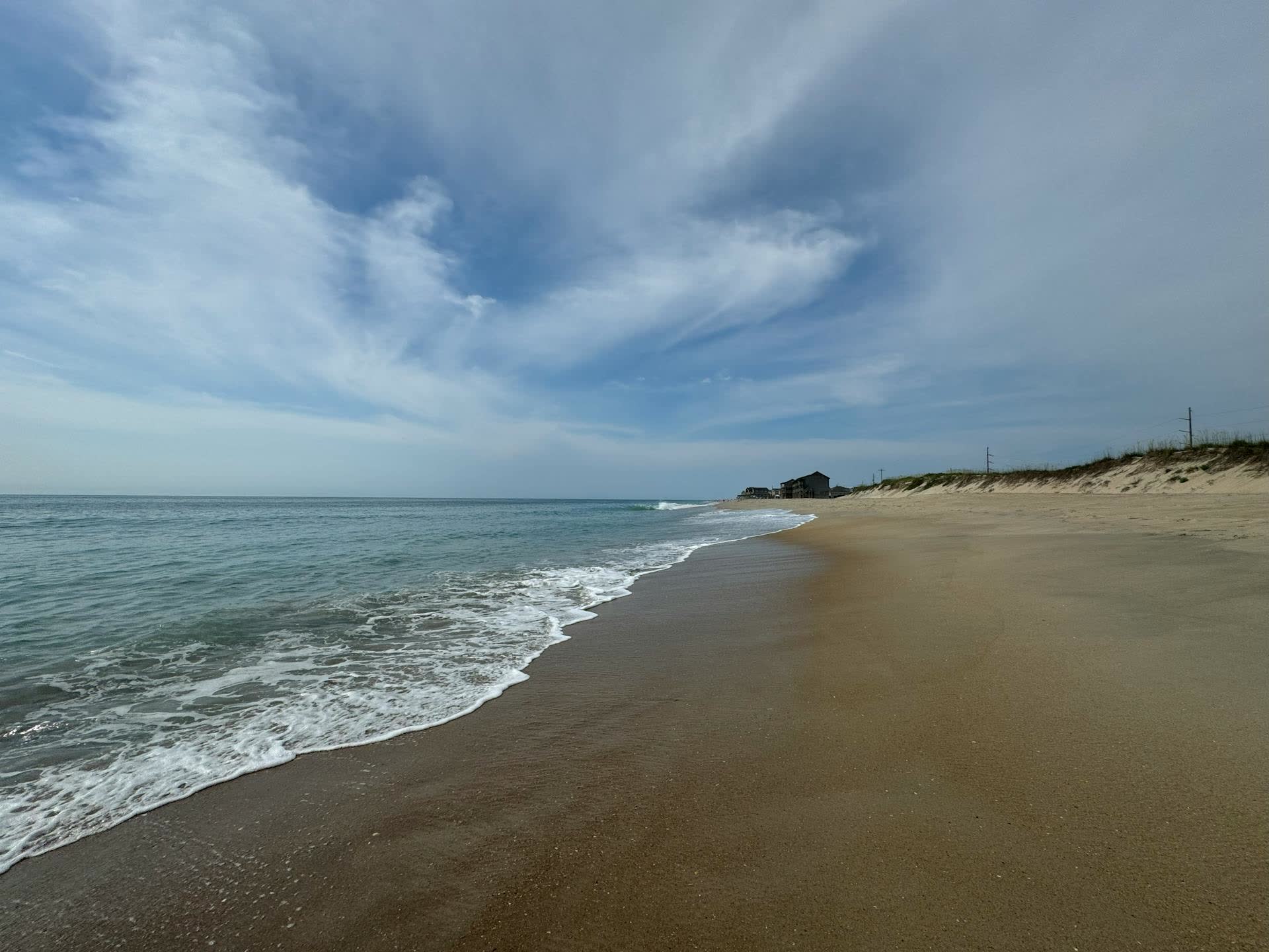Outer Banks shoreline at low tide, oceanfront rental houses on the horizon.